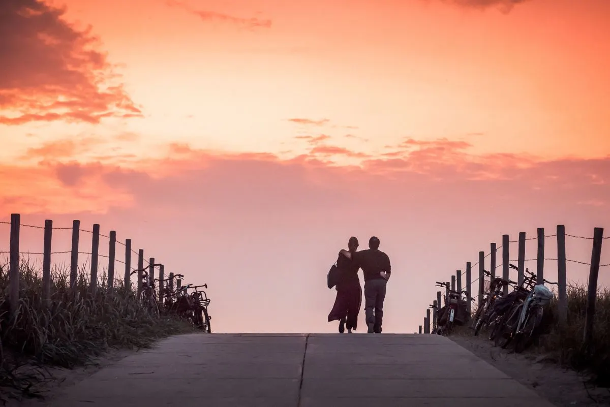 Twee mensen die bij zonsondergang samen over een strandpad lopen.